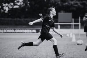 Meisje in zwart voetbaloutfit rent op het veld tijdens training bij Voetbalschool Groesbeek.