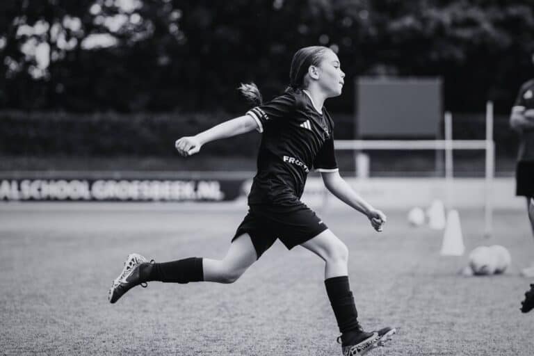 Meisje in zwart voetbaloutfit rent op het veld tijdens training bij Voetbalschool Groesbeek.