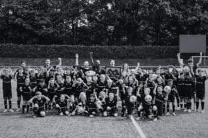 Groepsfoto van jonge voetballers en coaches op het veld bij Voetbalschool Groesbeek, vierend na een training of wedstrijd.
