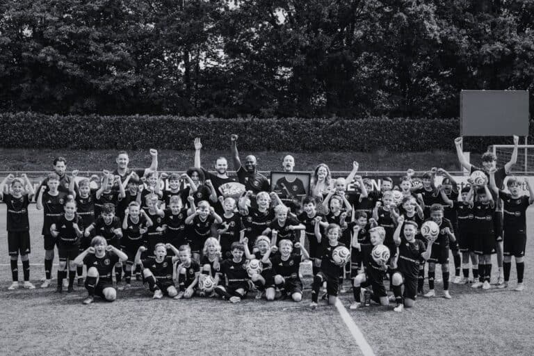 Groepsfoto van jonge voetballers en coaches op het veld bij Voetbalschool Groesbeek, vierend na een training of wedstrijd.