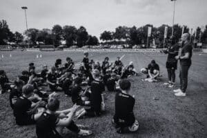 Voetbalschool Groesbeek kinderen tijdens training op het veld, instructeur geeft uitleg, sportieve sfeer, zomerse dag.