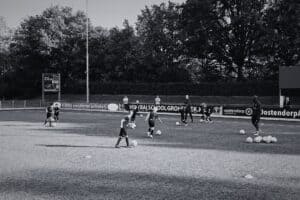 Voetbalschool Groesbeek training met jonge spelers op het veld, begeleid door coaches, tijdens een zonnige dag.